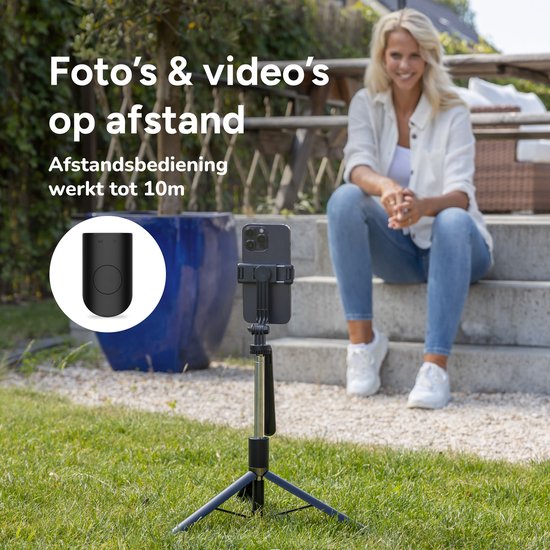 Vrouw zittend op trap, selfiestick met telefoon en zwarte afstandsbediening op gras.