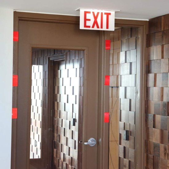 Deurposten met rode reflecterende tape, met een 'EXIT'-bord erboven.