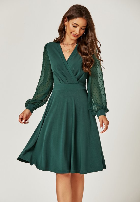 Model in een donkergroene midi-jurk met wikkelkraag en pofmouwen met stippen. De jurk heeft een A-lijn rok.