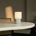Tafellamp met marmeren voet en linnen kap, op een lichte tafel.