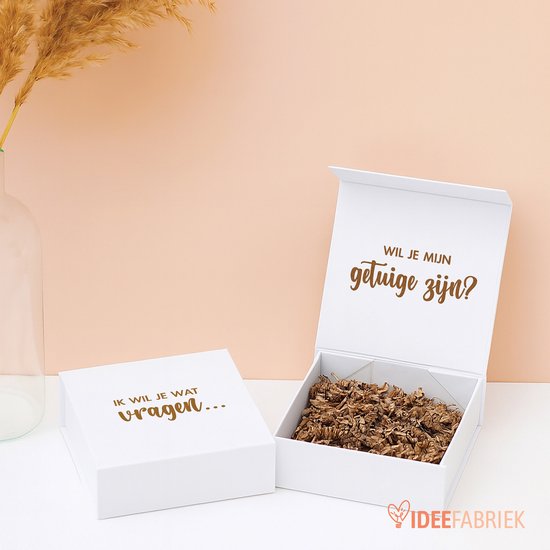 Boîte cadeau blanche ouverte avec le texte 'Veux-tu être mon témoin ?', remplie de rembourrage marron. Boîte fermée avec le texte 'Je veux te demander quelque chose...'