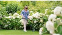 Vrouw met spijkerblouse gebruikt de Bosch grastrimmer in een tuin met witte bloemen.