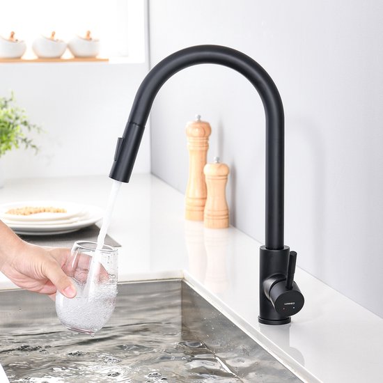 Zwarte keukenkraan met uittrekbare sproeikop, die water in een glas giet.