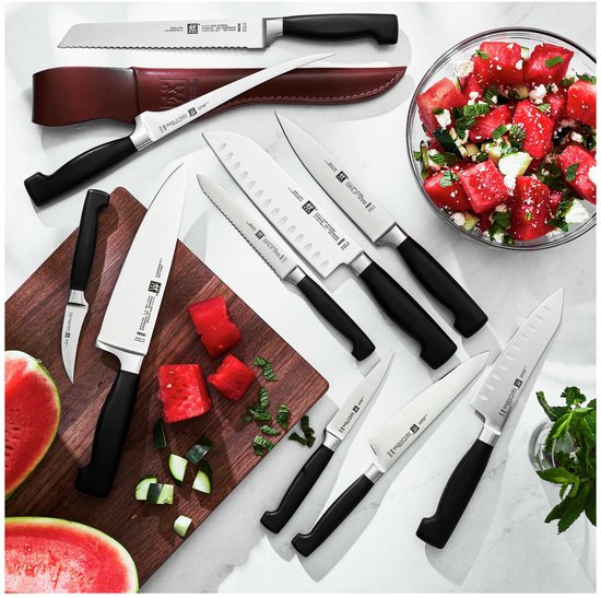 Een set van zeven ZWILLING messen, waaronder een broodmes met kartels, op een snijplank met stukken watermeloen en munt.