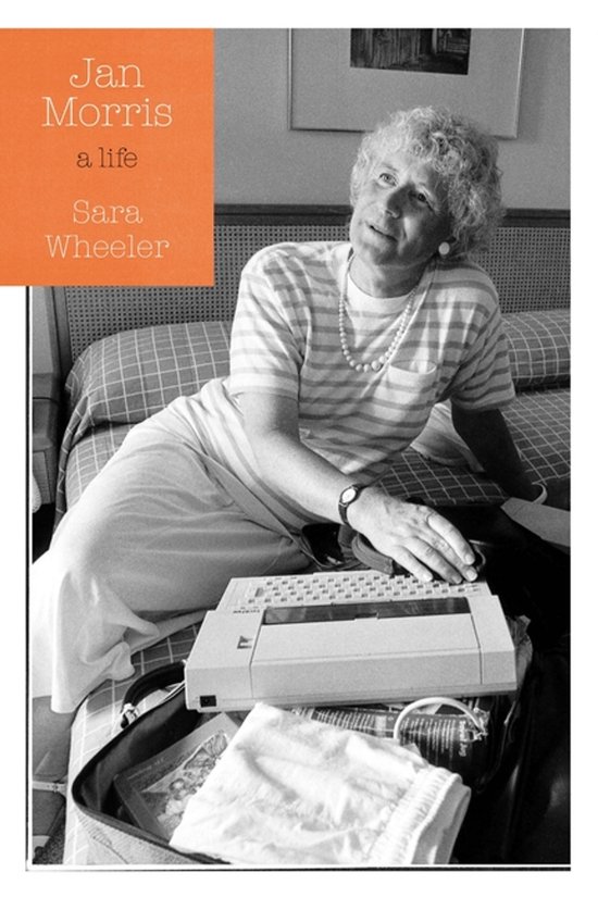 Jan Morris: een leven - Sara Wheeler. Een vrouw zit op een bed met een typemachine.