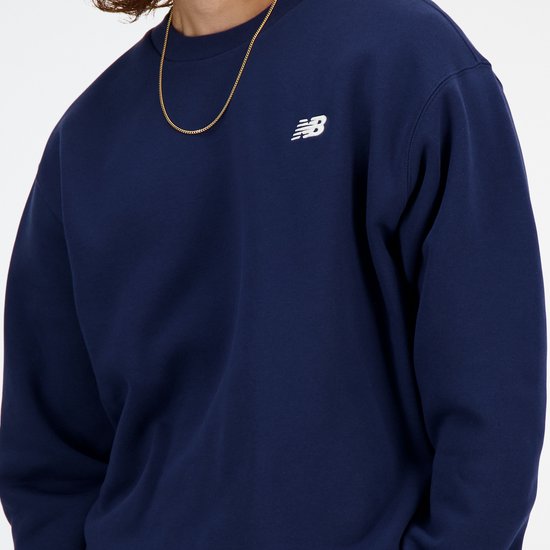 Close-up van donkerblauwe New Balance trui met wit logo op de borst.