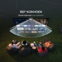 Groep mensen kijken ontspannen naar een projectiescherm met 160 graden kijkhoek, in een tuin op zitzakken.