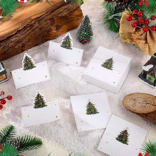 Kerstboom-plaatskaartjes met gouden sterren op een witte kaart, omringd door kerstdecoratie.