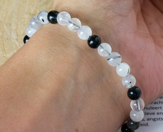 Armband met afwisselend zwarte toermalijn en heldere kwartskralen, om een pols gedragen.