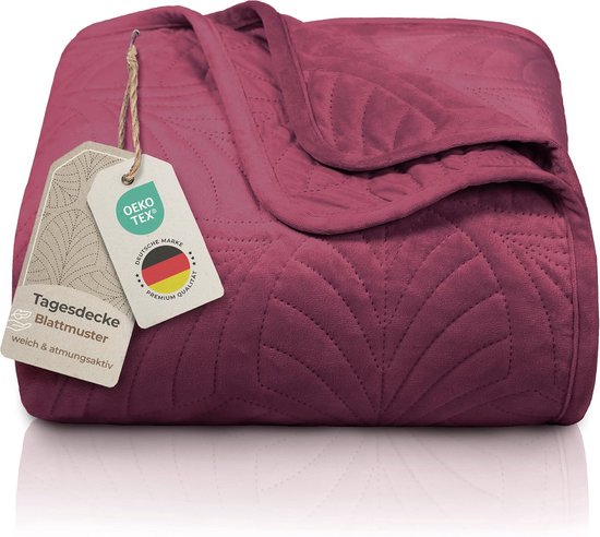 Bordeauxrode sprei (240x260 cm) met een zacht fluweelachtig materiaal en een gestikt bladmotief. Merkje met 'Tagesdecke Blattmuster' en OEKO-TEX certificering.