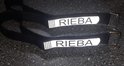 Twee zwarte broekklemmen met gespen en een reflecterend 'RIEBA' logo.
