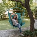 Vrolijke vrouw in gestreepte top en jeans in turquoise hangstoel, bungelend aan een boomtak in de tuin.