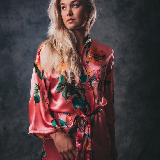 Lange koraalrode satijnen kimono met veelkleurige bloemenprint en ceintuur. Model met blonde haren kijkt weg.