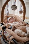 Baby in beige outfit en mutsje slaapt in een bruine wipstoel met speelboog.