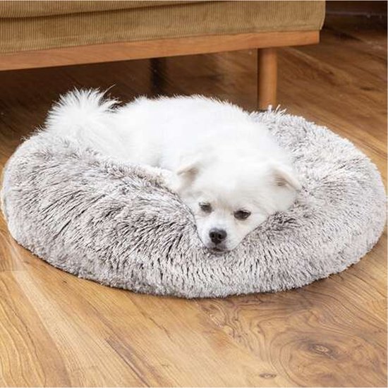 Kleine witte hond op een ronde, zachte, grijze mand.