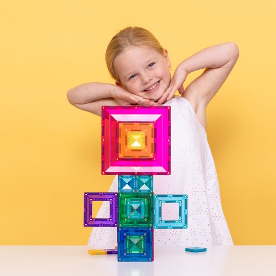 Meisje met blond haar in een witte jurk die een kleine, gekleurde, magnetische Connetix constructie vasthoudt.