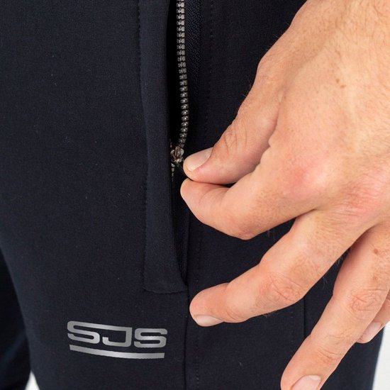 Close-up van een hand die een rits op een donkerblauwe joggingbroek sluit. Het 'SJS' logo is zichtbaar.