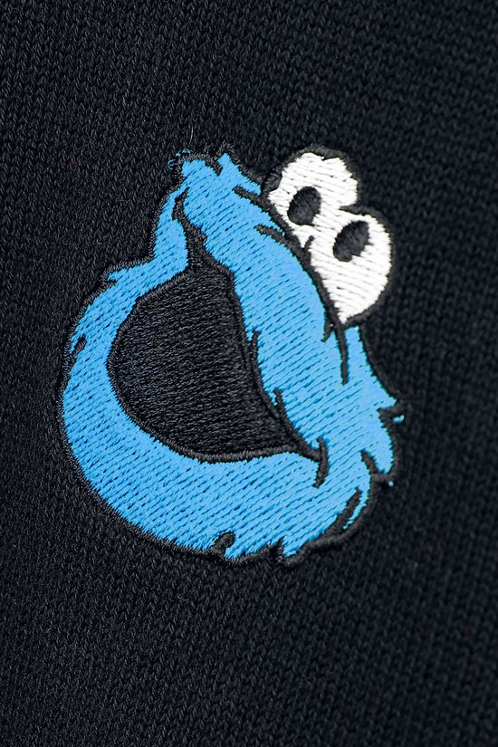Close-up van een geborduurd Cookie Monster-logo in blauw en wit op een zwarte gebreide trui.