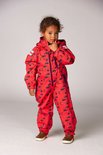 Meisje in rood regenpak met donkerblauwe bloemenprint, staand met de hand bij de kin.