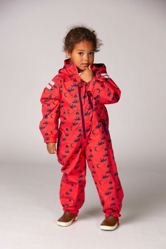 Meisje in rood regenpak met donkerblauwe bloemenprint, staand met de hand bij de kin.