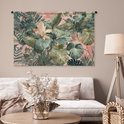 Een wandkleed met een weelderige tropische bladerenprint in groen en roze, hangend boven een witte bank in een neutrale woonkamer.