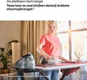 Vrolijke vrouw in rood shirt en spijkerbroek, strijkt met zwart Braun CareStyle 3 strijkijzer over rood laken. Verwijst naar 'DoubleSteam-technologie'.