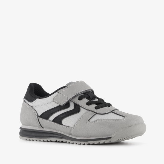 Grijze sneaker met zwarte zigzagstrepen, klittenbandsluiting en zwarte accenten.