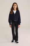 Meisje draagt een zwarte flared legging en een donkerblauw pluizig vest met knopen.