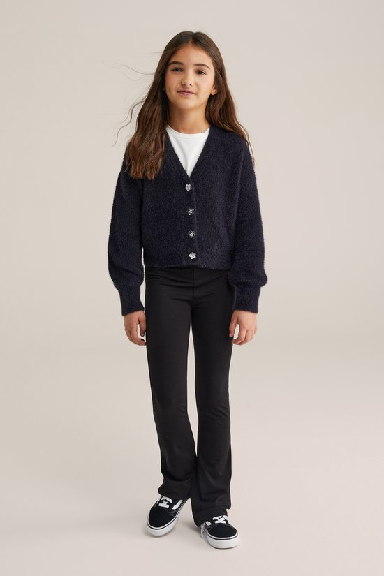 Meisje draagt een zwarte flared legging en een donkerblauw pluizig vest met knopen.