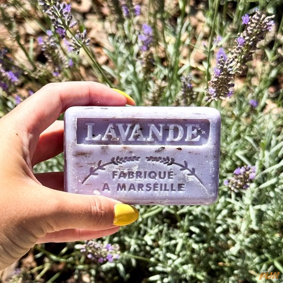 Paarse lavendelzeep met de tekst 'LAVANDE FABRIQUÉ A MARSEILLE', in een hand met gele nagellak.