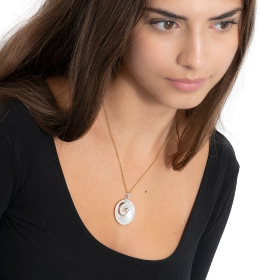 Une femme aux longs cheveux bruns porte une chaîne dorée avec un pendentif en nacre, un croissant de lune et un petit diamant.