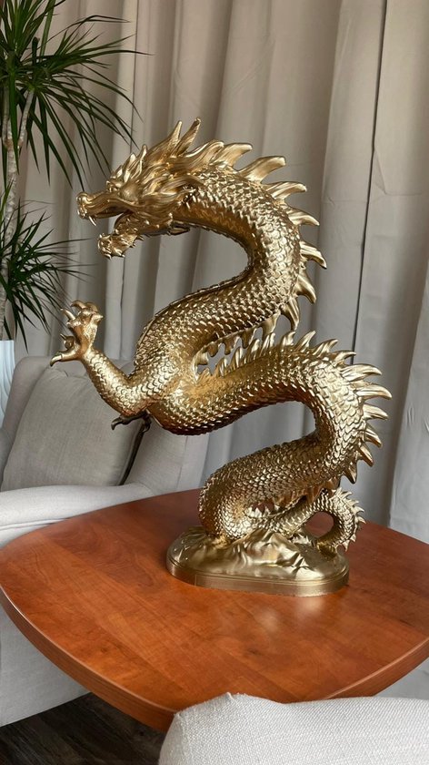 Gouden draak ornament op een tafel, met bladeren en gordijnen op de achtergrond.