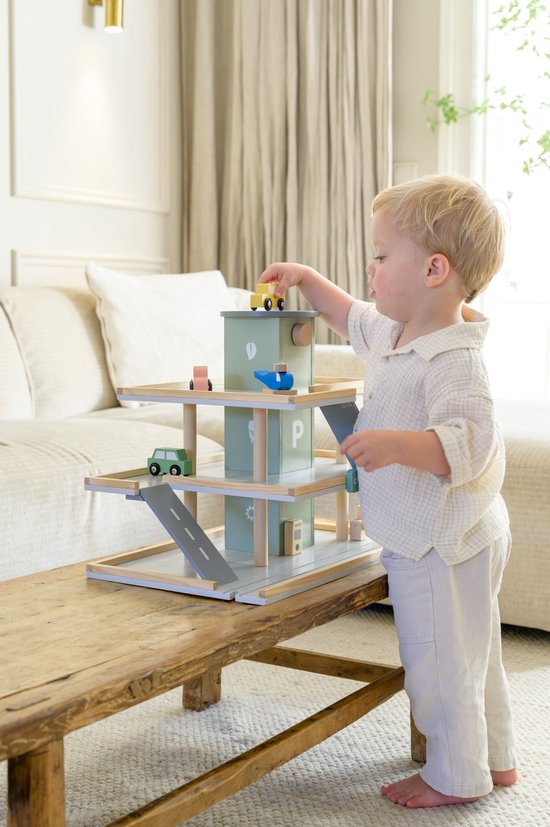 Jongetje met blond haar, in linnen kleding, speelt met een pastelgroene houten speelgoedgarage.