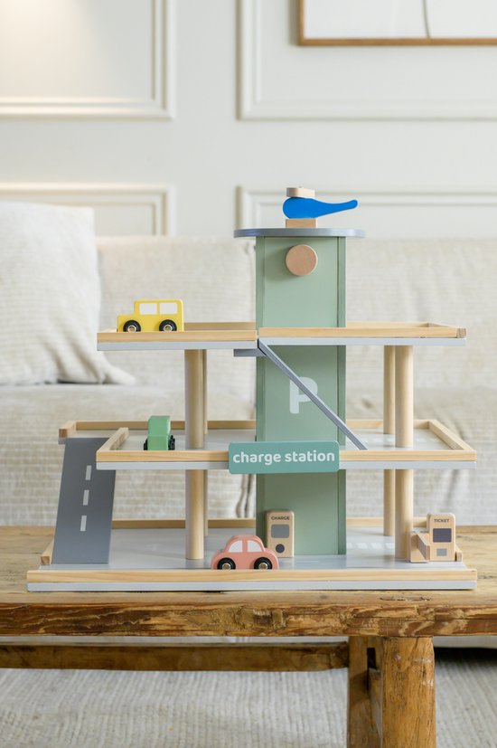 Houten speelgoedgarage in pastelgroen met 3 verdiepingen, auto's, helikopter en laadstation, op een houten tafel.