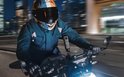 Motorrijder met veelkleurige helm en blauwe jas filmt met actioncam op motor.