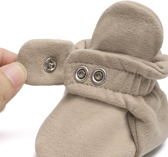Close-up van een taupe baby slof, een hand sluit de drukknoopjes.