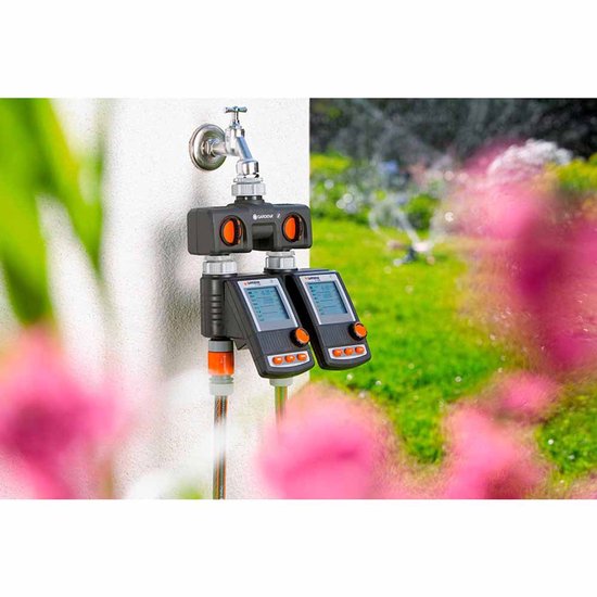 Gardena waterverdeler met kraan, twee slangen en twee digitale timers met oranje knoppen. Op de achtergrond een tuin.