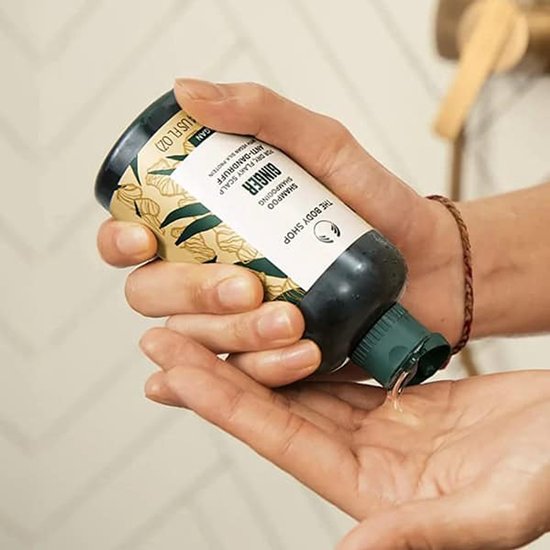 Main tenant le shampooing anti-pelliculaire au gingembre The Body Shop, bouteille avec motif gingembre, 250ml.