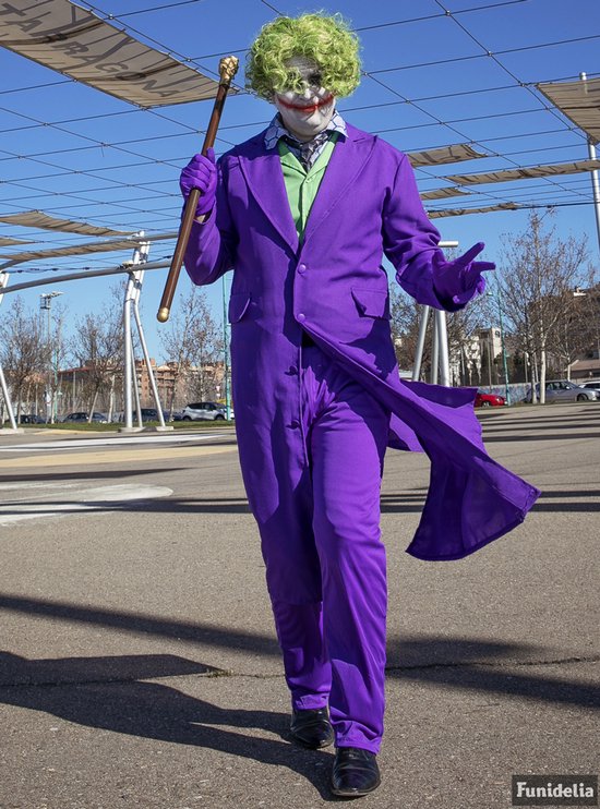 De Joker in paars kostuum met groene pruik en wandelstok loopt buiten.