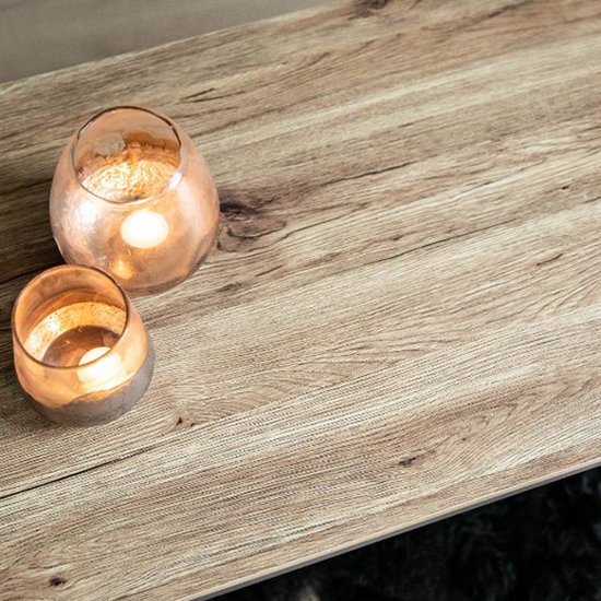 Close-up van het licht houten tafelblad met een grof patroon. Twee glazen windlichten met brandende kaarsen.