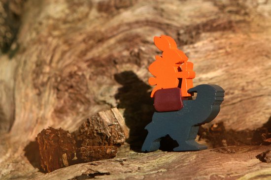Houten speelfiguur van een blauwe dingo met een oranje konijn op zijn rug, op een houten achtergrond.