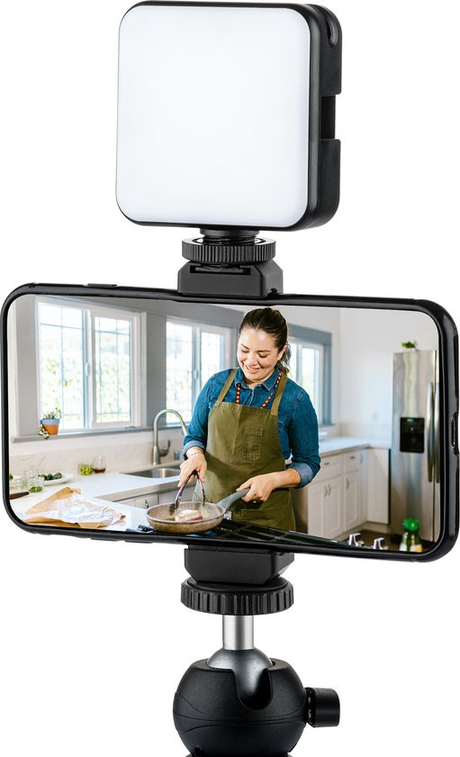 Een smartphone op een statief met een MOJOGEAR LED lamp erboven. De smartphone toont een vrouw in een keukenschort die kookt.