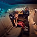 Lachend meisje in een donkergrijs Maxi-Cosi autostoeltje, vastgegespt in de achterbank van een auto.