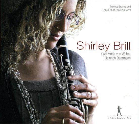 Shirley Brill met bril en parelketting, houdt een klarinet vast met de tekst 'Shirley Brill'