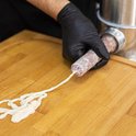 Handen met zwarte handschoenen vullen een darm met vlees van een worstmachine.