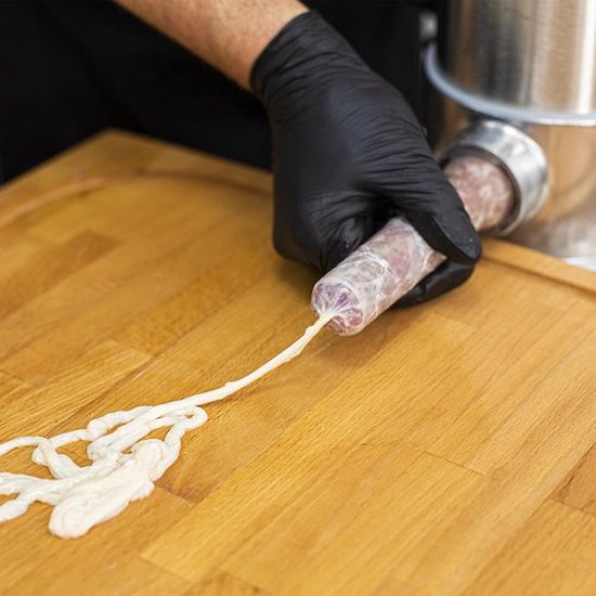 Handen met zwarte handschoenen vullen een darm met vlees van een worstmachine.