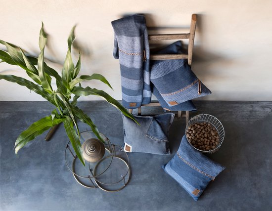 Blauwe en grijze kussens en plaids in verschillende stijlen, gerangschikt rond een houten ladder.