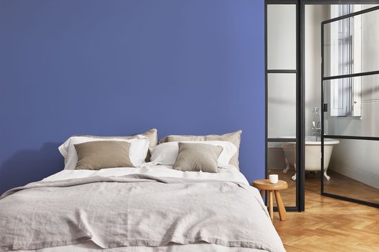 Slaapkamer met een groot bed, linnen beddengoed en een blauwe muur.