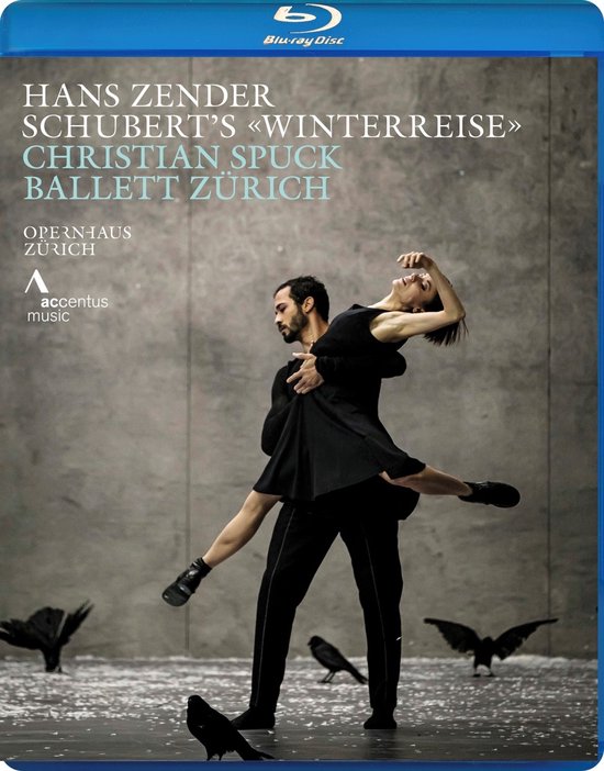 Een mannelijke danser met een zwarte outfit draagt een vrouwelijke danseres met een zwarte jurk. Achter hen vliegen raven.
