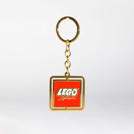 Gouden sleutelhanger met een draaibare, rode bedel met het LEGO System logo in wit en geel.